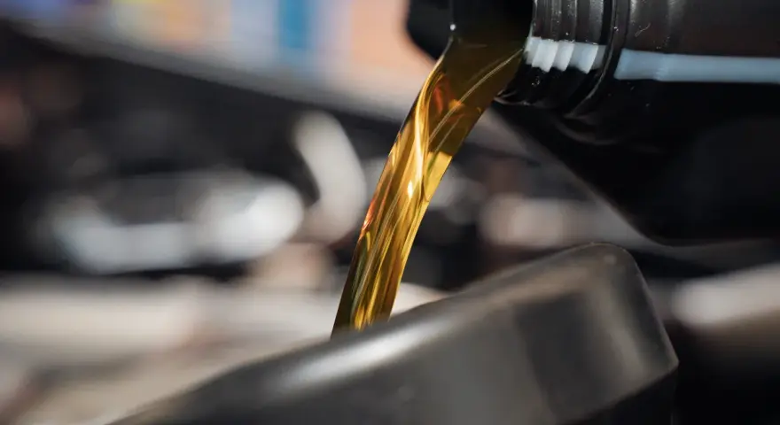 Goldfarbenes Motoröl fließt aus einem schwarzen Behälter in einen dunklen Trichter.